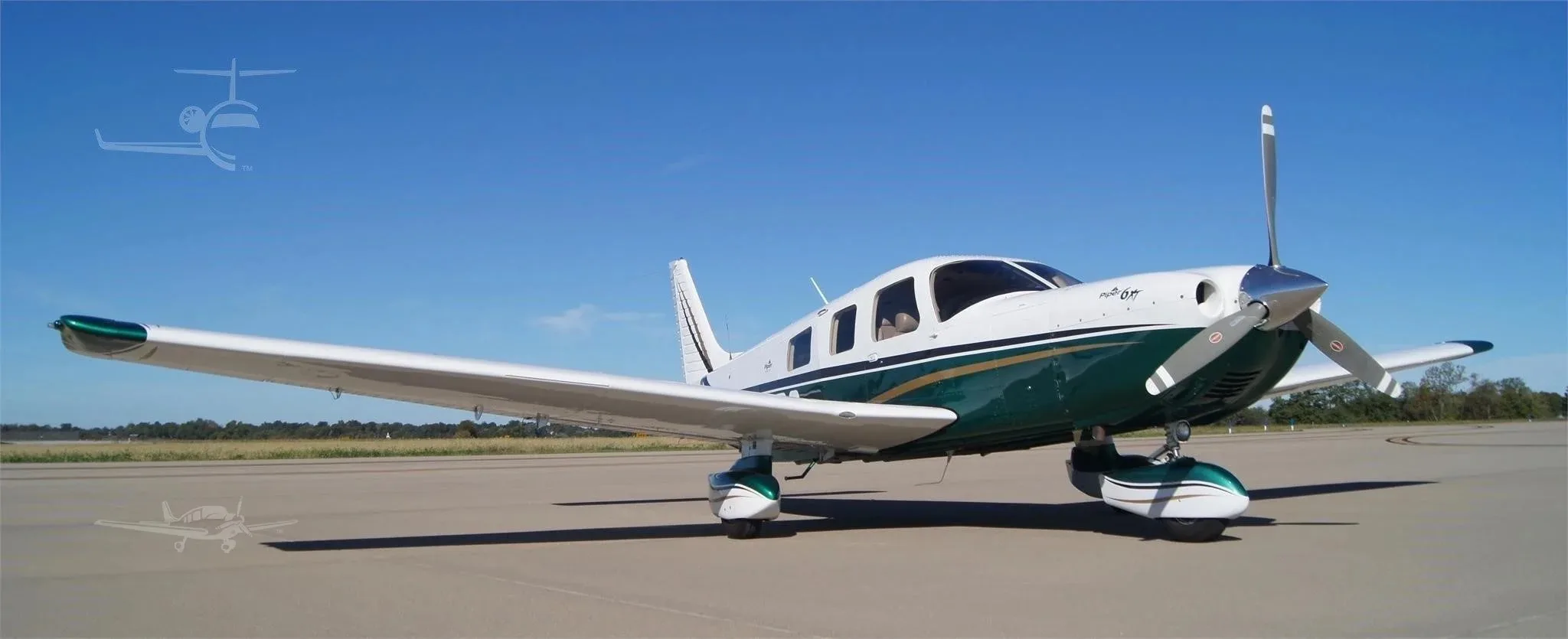 A front-side low-angle view of the white and green Piper 6XT (N529RG) parked on an airfield under a clear blue sky.