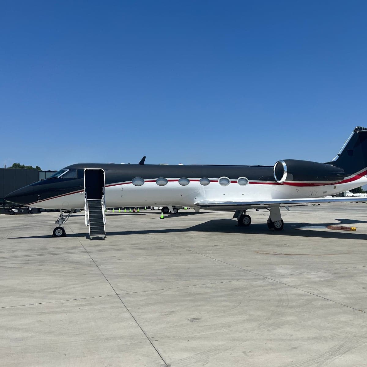 Side view of a black and white Gulfstream jet with airstair deployed on the ramp.