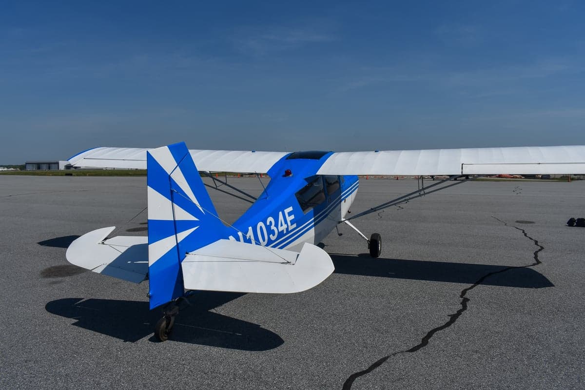 Front side view of a blue and white aircraft with tail number N1034E in front of a hangar.