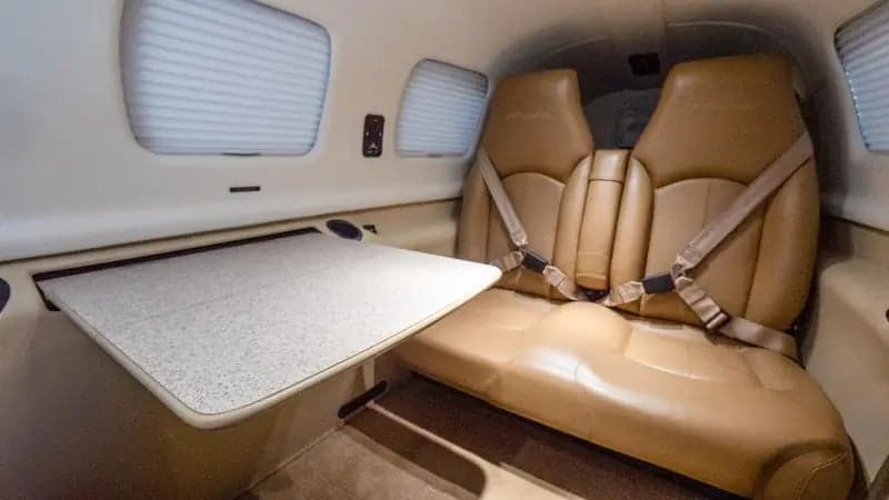 The tan leather passenger seats and a fold-out table in the cabin interior of a Piper M-class aircraft.