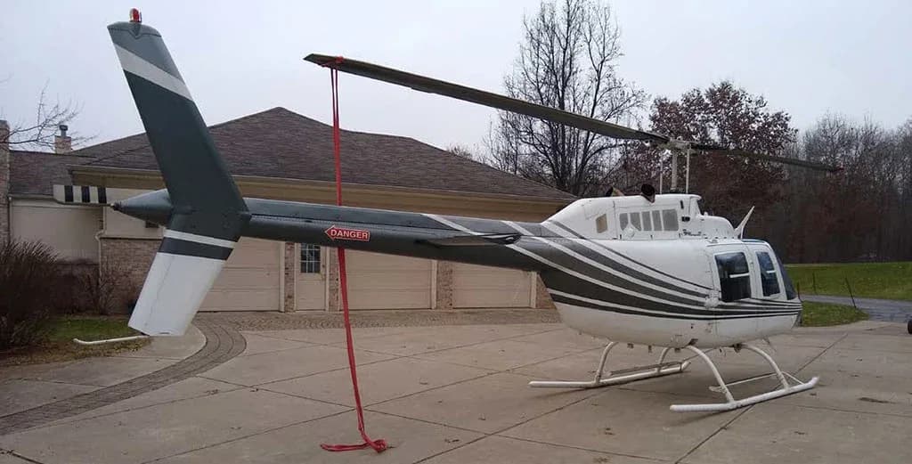 Rear-side view of a white helicopter with dark grey stripes, showing the tail boom and rotor.