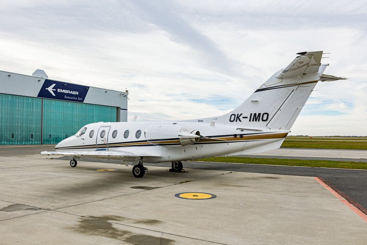 Beechjet 400A aircraft with registration OK-IMO parked in front of an Embraer hangar.