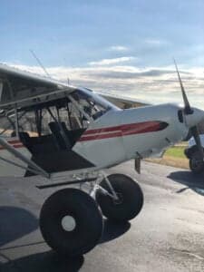 A white and red Piper Cub sits on the tarmac.