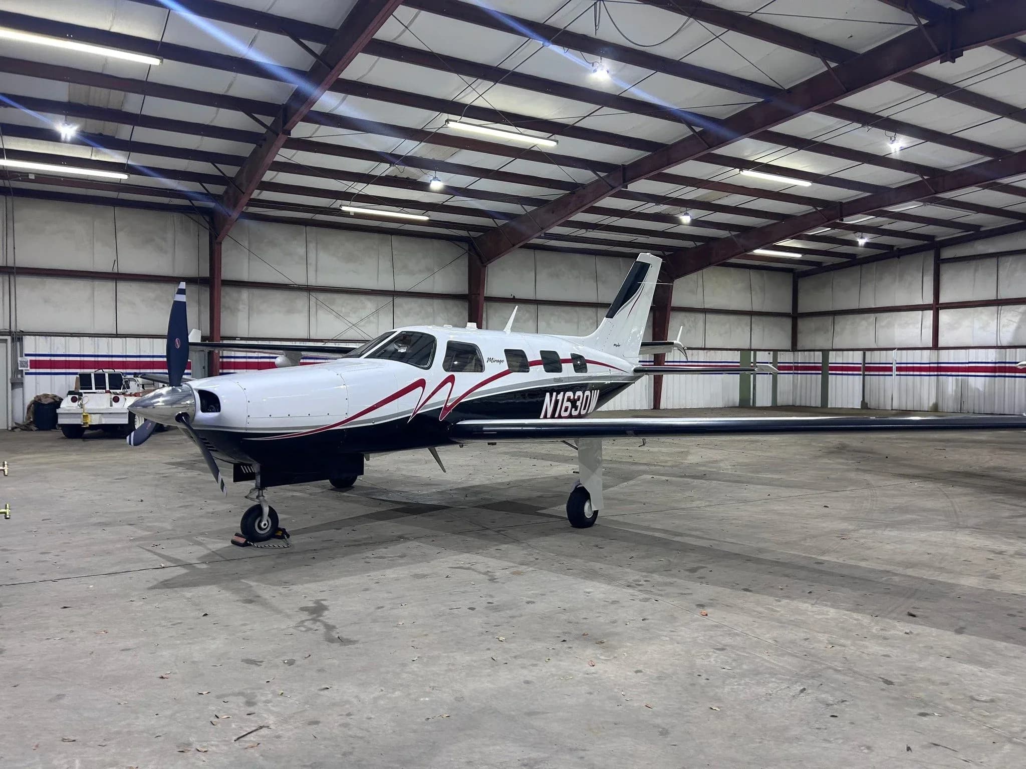 A Piper aircraft with a white and black paint scheme is parked inside a hangar.