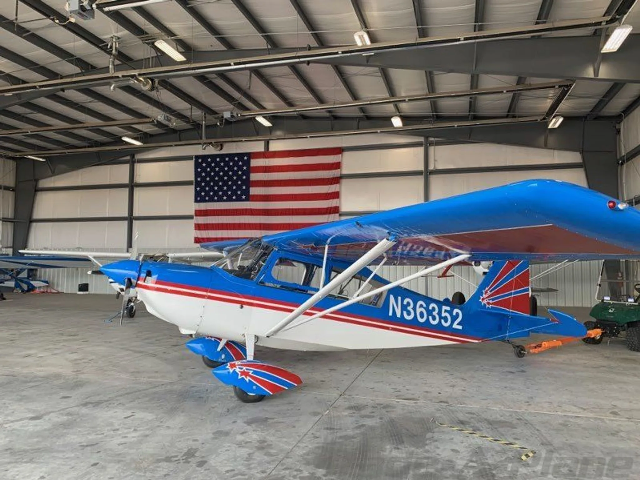 A blue and white high-wing aircraft with red stripes and tail art, registration N36352, parked in a hangar with an American flag.