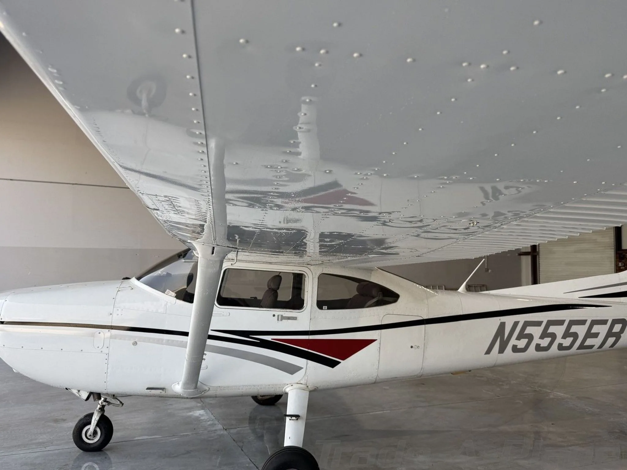 A side view of the white Cessna 182 Skylane fuselage and wing, showing the N-number and paint scheme, inside a hangar.