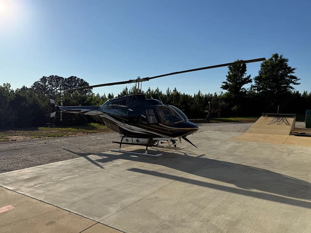 A black and gold helicopter, N887EH, is parked on a concrete pad under a clear blue sky.