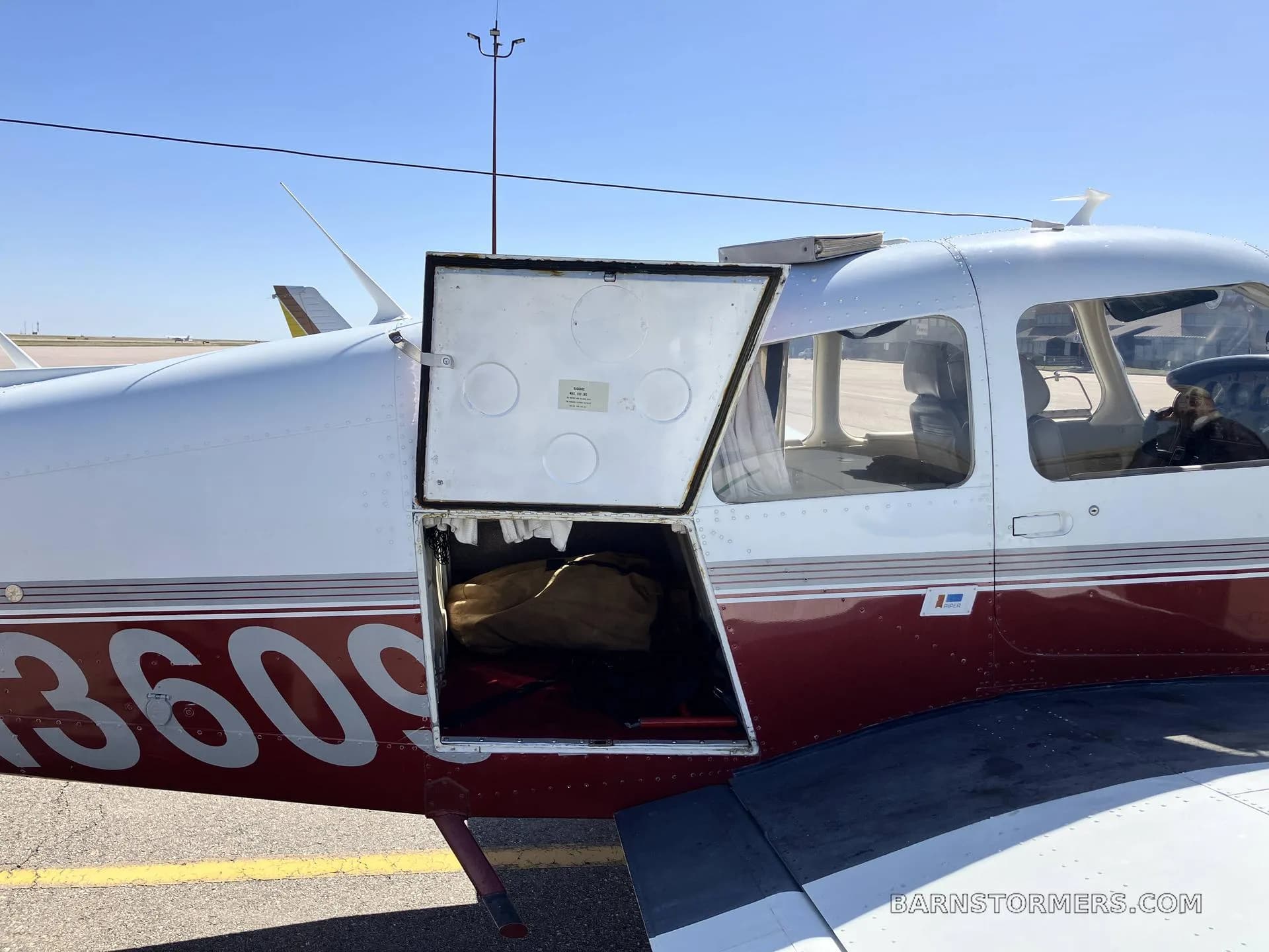 A close-up of the white and maroon aircraft's fuselage with the baggage compartment door open, revealing a bag inside.
