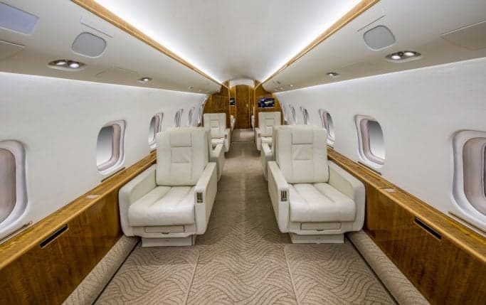 Aircraft interior featuring white leather seats and wood paneling.