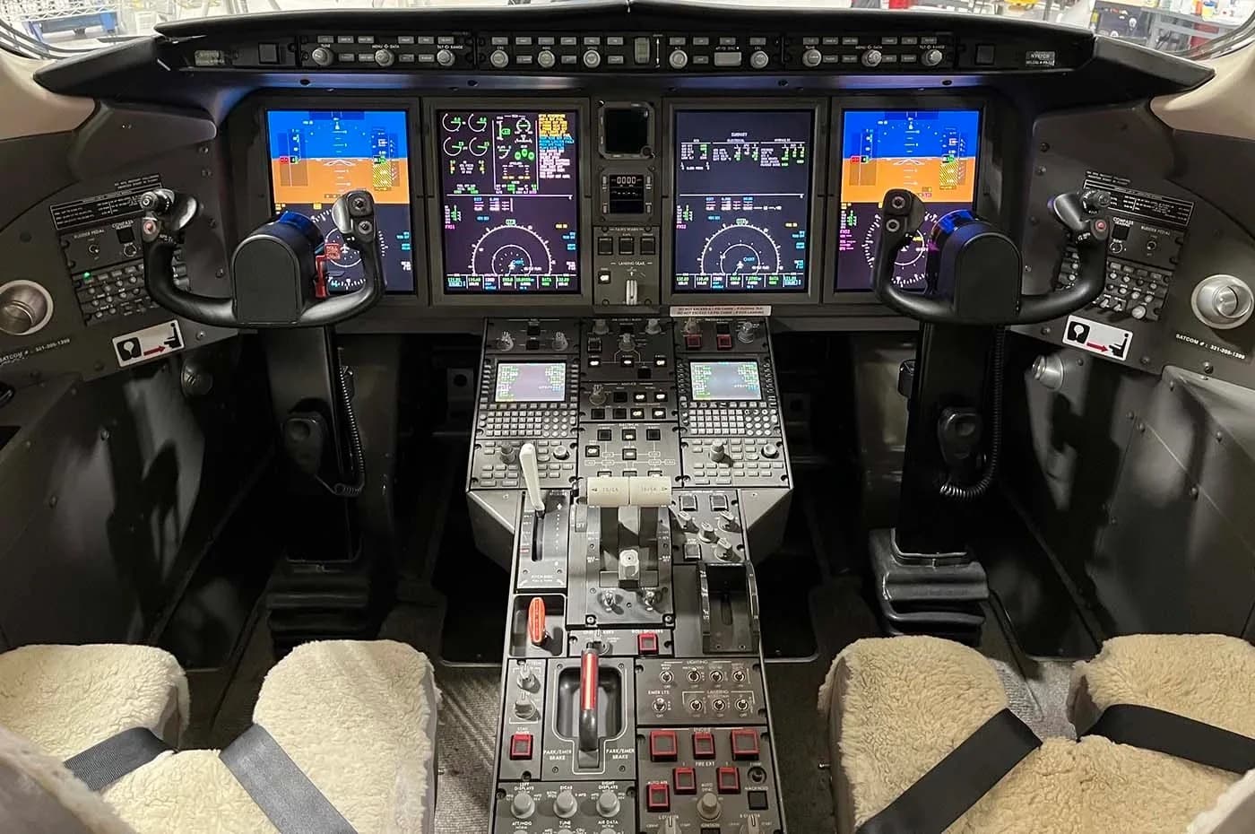 The modern cockpit of a business jet with multiple digital displays and control yokes.