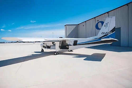 A white and blue twin engine aircraft is parked in front of a hangar on a sunny day.