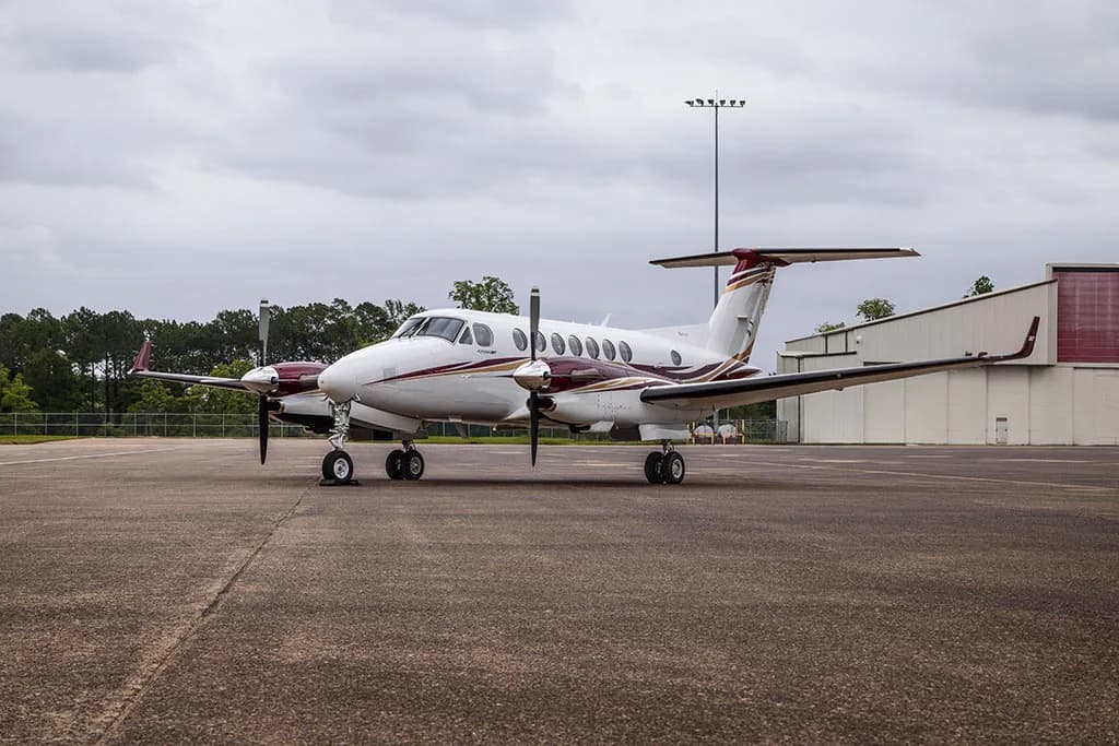 A white and maroon twin-engine turboprop aircraft, N367TP, parked on an airfield with hangars in the background.