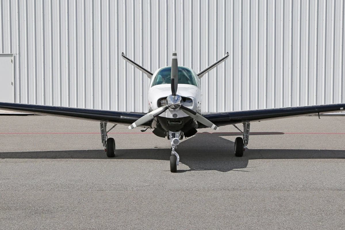 Close-up front view of a Beechcraft Bonanza aircraft on the ground in front of a hangar.