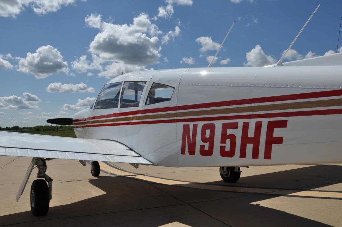 A close-up of the white aircraft's fuselage showing the red and gold stripes and registration N95HF.