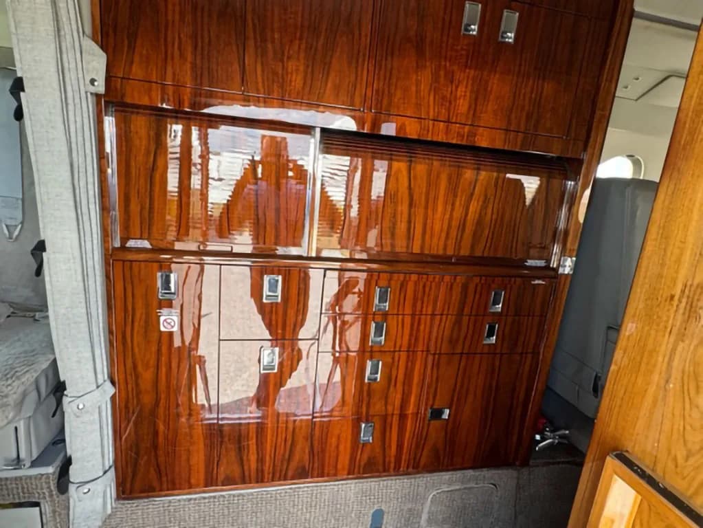 Close-up of highly polished dark wood cabinetry with silver handles and reflective surfaces inside a business jet cabin.