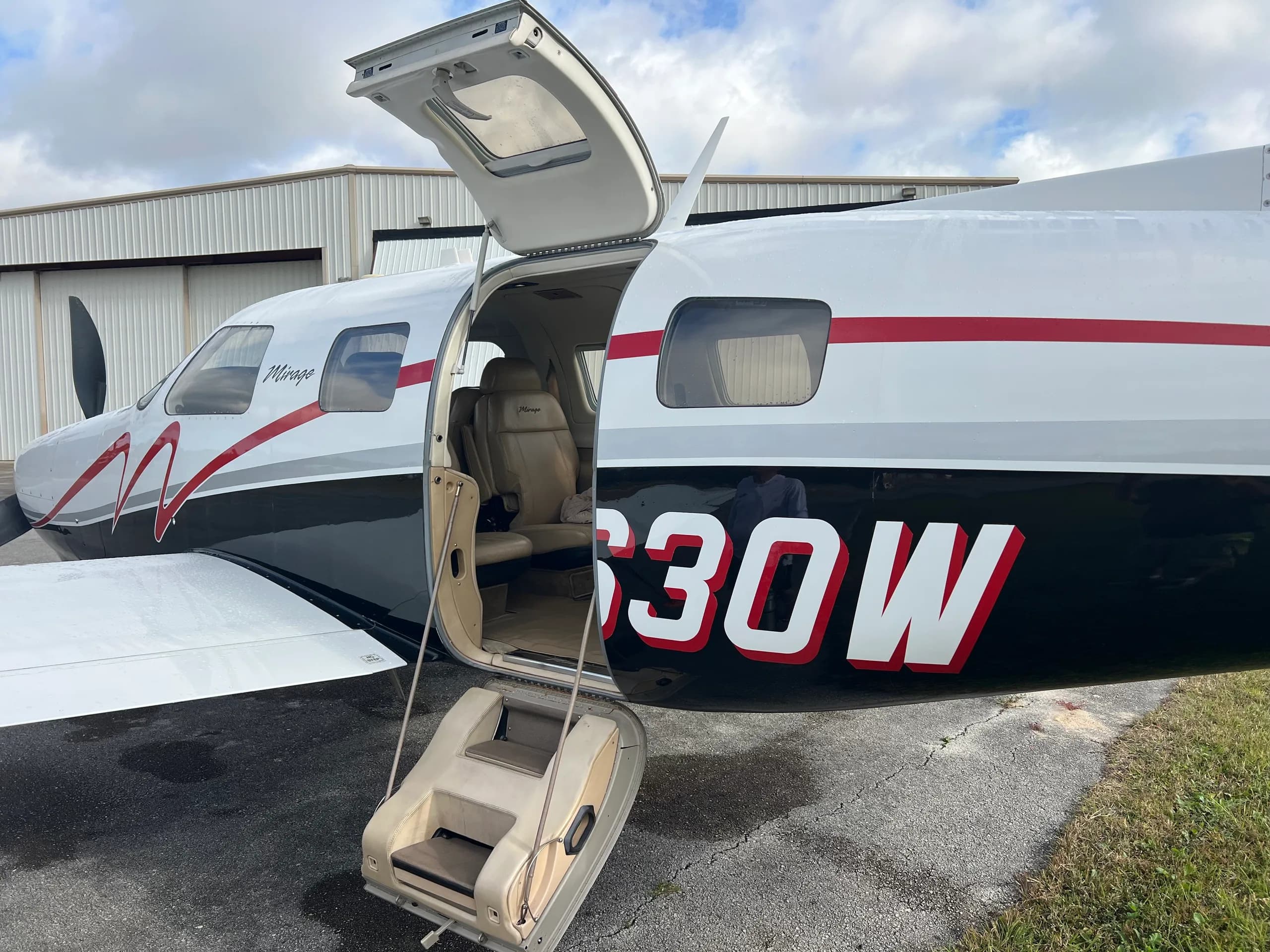 A close-up of the white and black Piper Mirage N1630W on an airfield, with its passenger door open and steps extended.