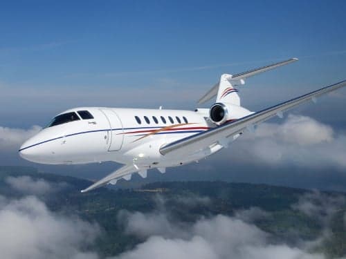 A white jet with red and blue stripes flies through the air above the clouds.