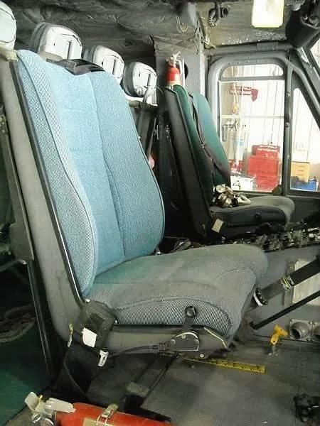 A close-up view of the blue and grey pilot's seat in a helicopter cabin, with a fire extinguisher visible on the floor.