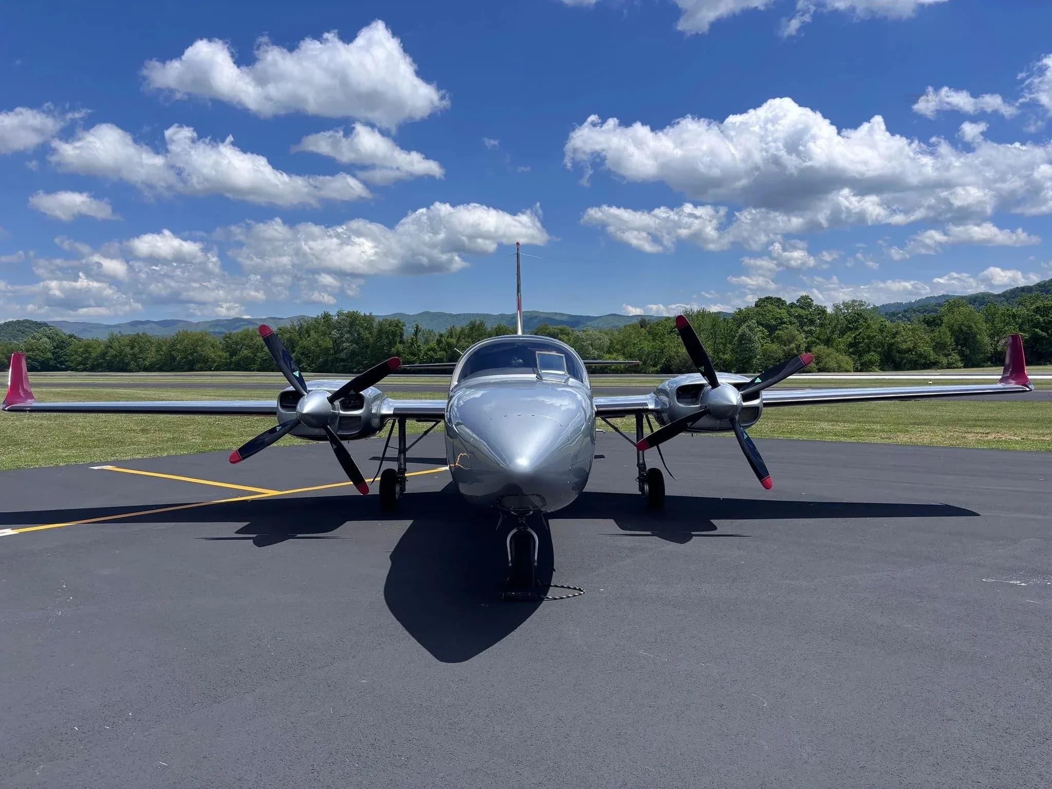 A head-on view of a silver and red twin-engine Aerostar aircraft (N702PG) parked on an airfield.