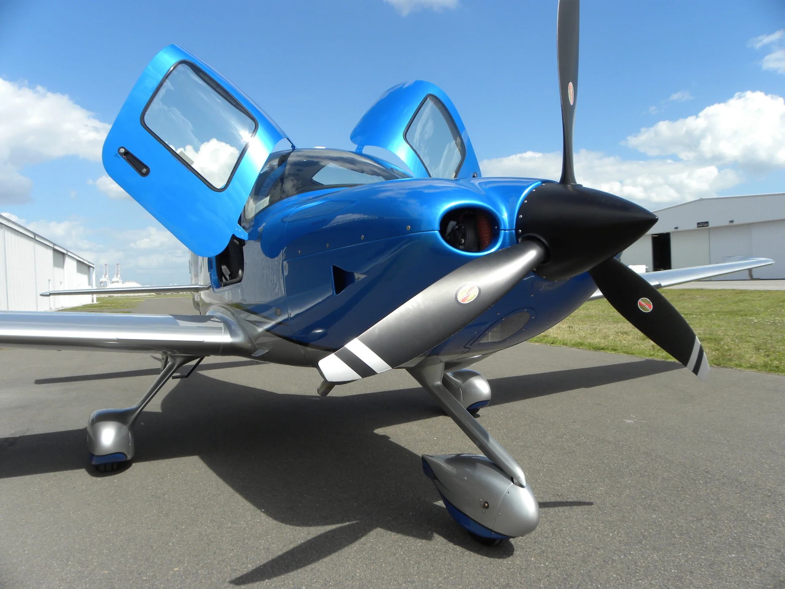 A blue and silver Cirrus SR22 aircraft with its gull-wing doors open, parked on an asphalt ramp.