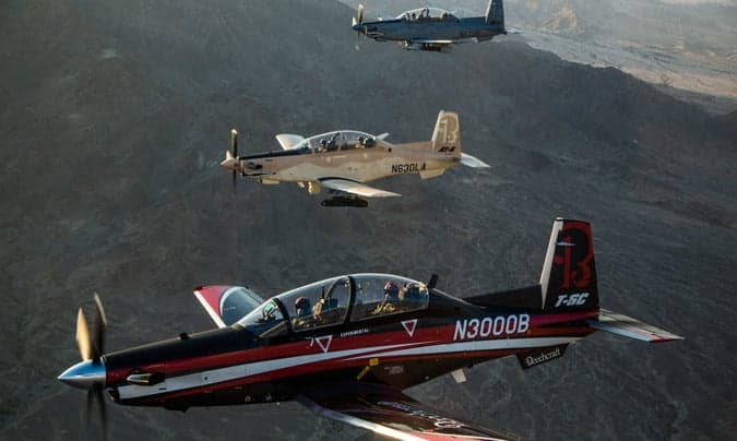 Three Beechcraft T-6C Texan II aircraft in flight over a mountainous landscape.