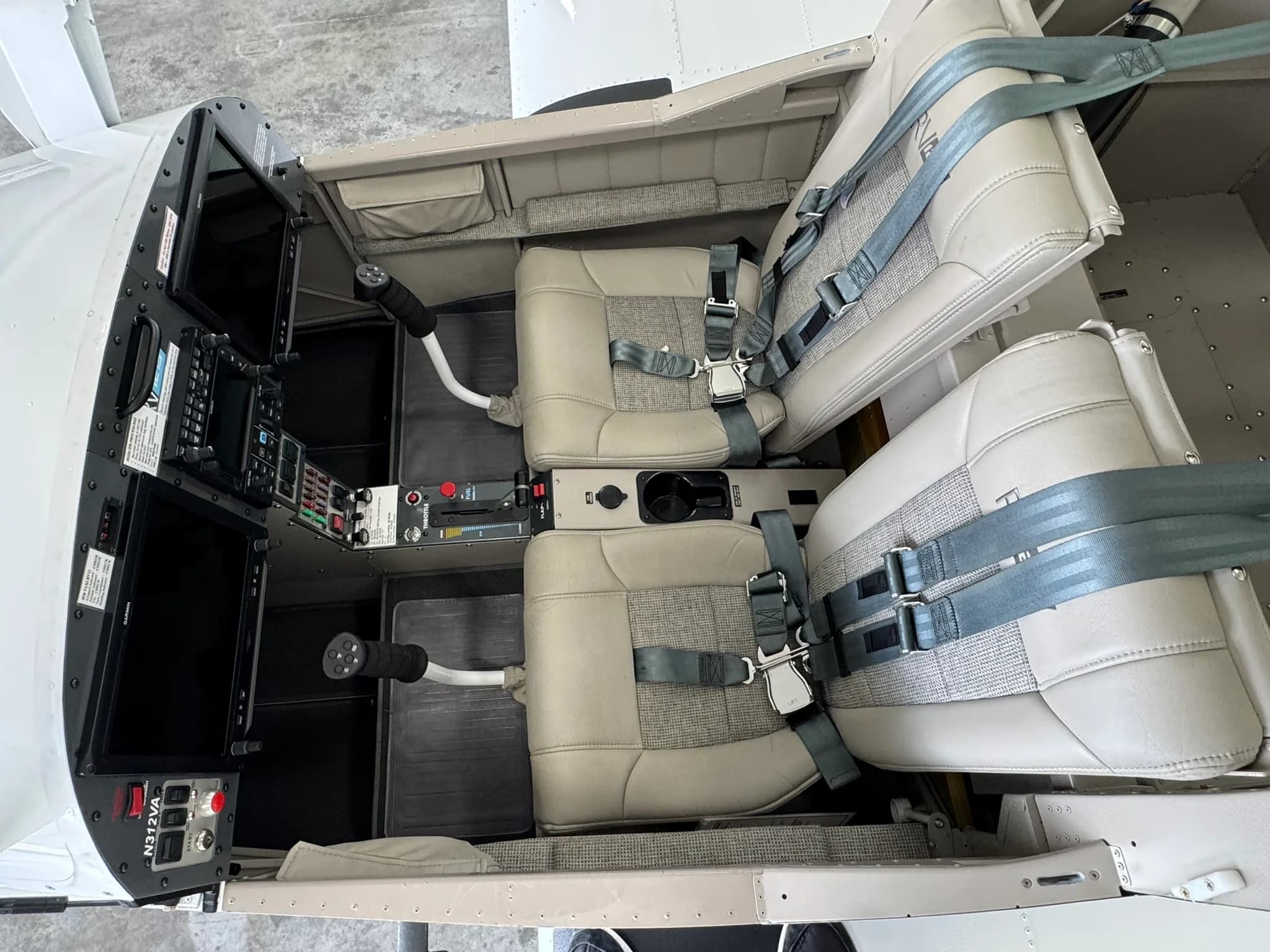 An overhead view of the aircraft cockpit, showing two beige seats, dual screens, and central controls.