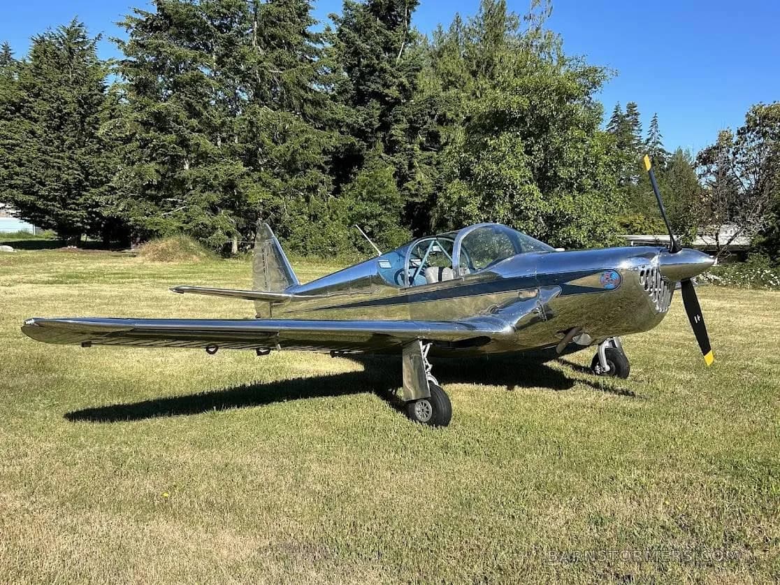 A polished silver single-engine propeller aircraft with a distinctive grille on the nose is parked on a grassy field.