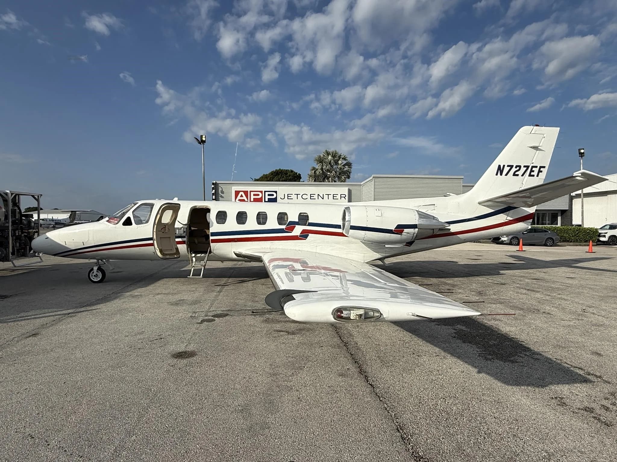 A white Cessna Citation business jet (N727EF) with its main door open, parked on an airfield next to a fuel truck.