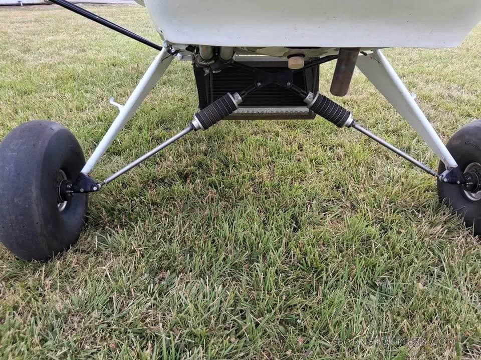 A close-up view of the robust landing gear and large tires of a white experimental aircraft on a grassy field.