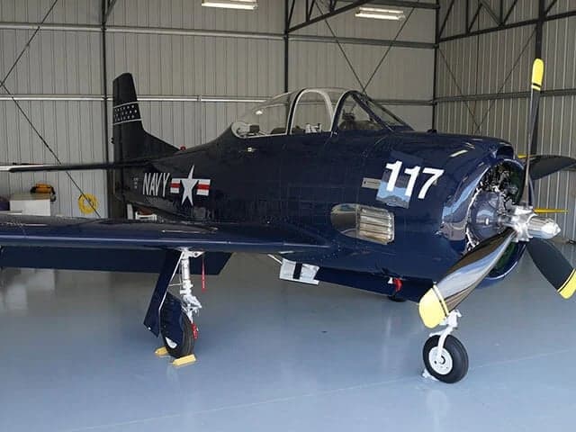 A dark blue US Navy AD-5 Skyraider with "117" on the cowling, parked inside a hangar.