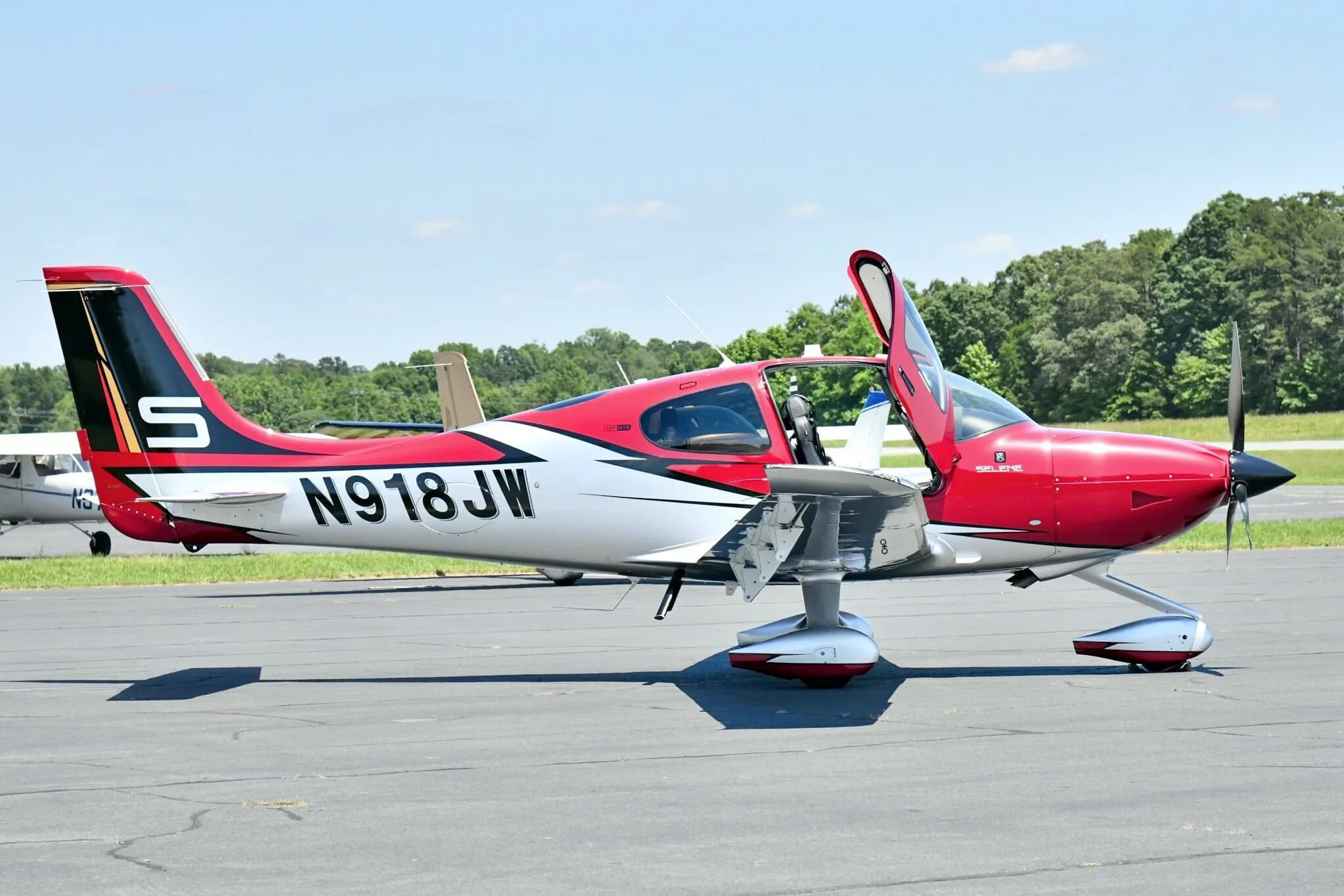 A red and white Cirrus SR22T aircraft with registration N918JW parked on an airfield with its doors open.