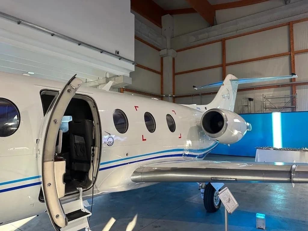 A white business jet with blue stripes has its main cabin door open, revealing the steps and interior, parked in a hangar.