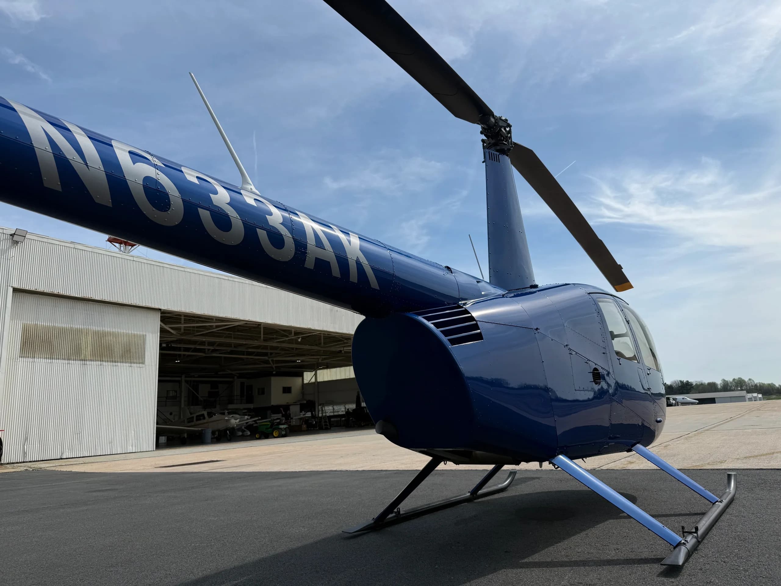 A close-up view of the tail boom and rotor of a blue Robinson R44 helicopter, N633AK, parked near a hangar.