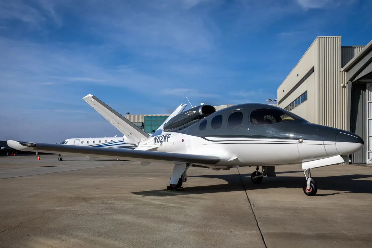A three-quarter front view of a white and dark grey Cirrus Vision Jet (N82WF) parked outside a hangar.
