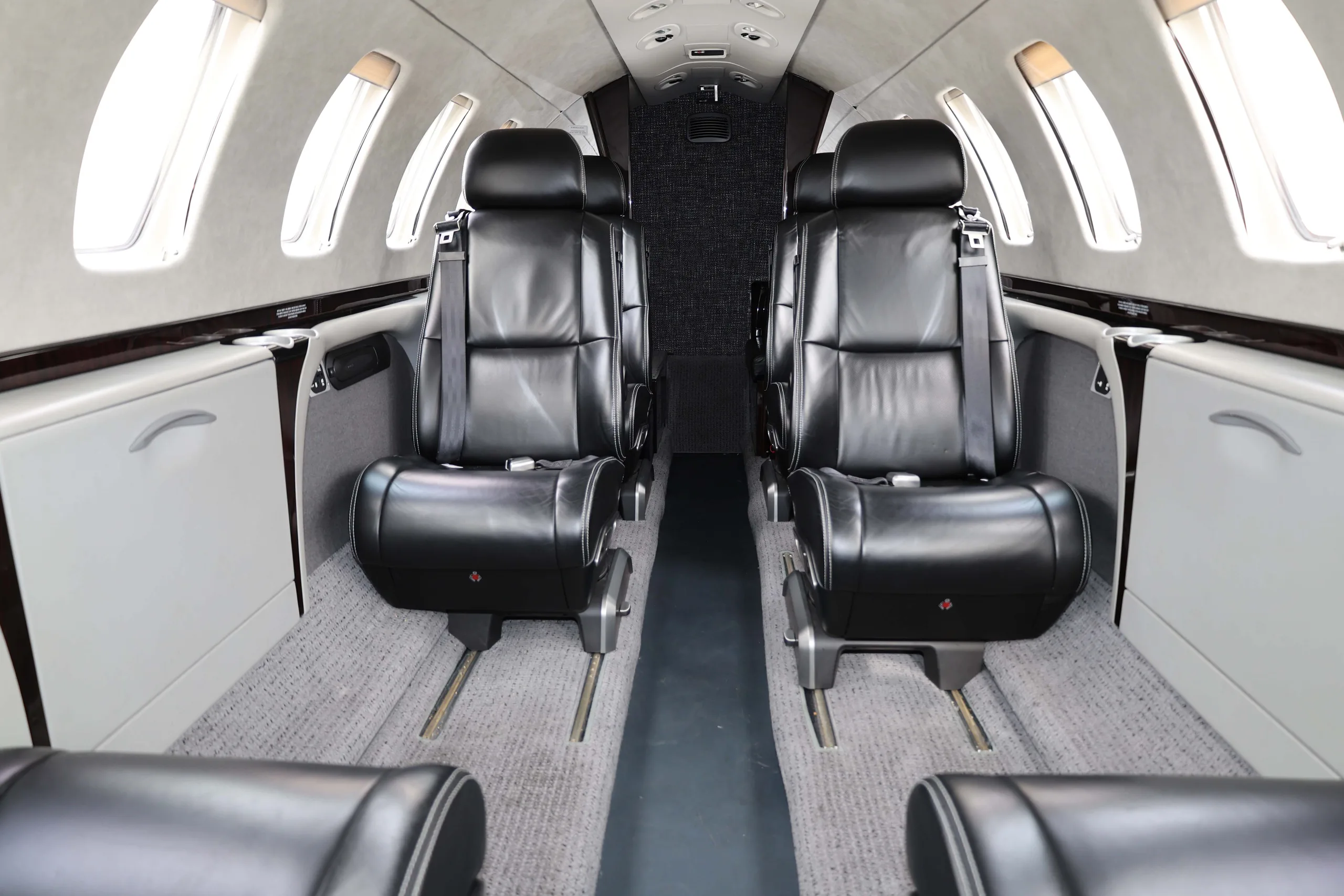 The interior cabin of a business jet, featuring black leather seats arranged in a club configuration with a light grey carpet.