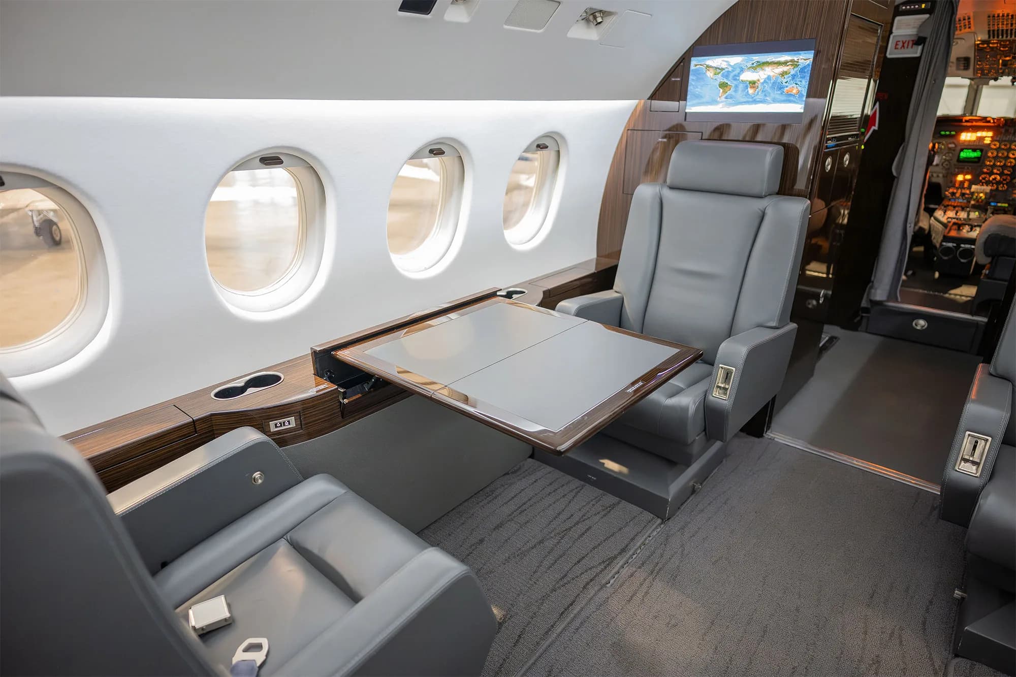 View of the aircraft interior with gray leather seats, a table, and a monitor.