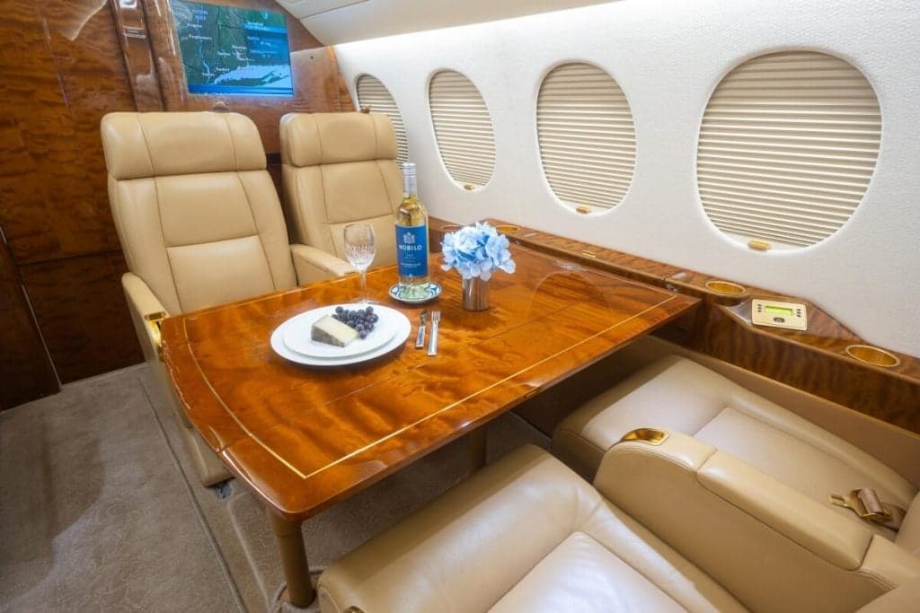 The aircraft's interior features tan leather seats, wood accents, and a laptop on a table.