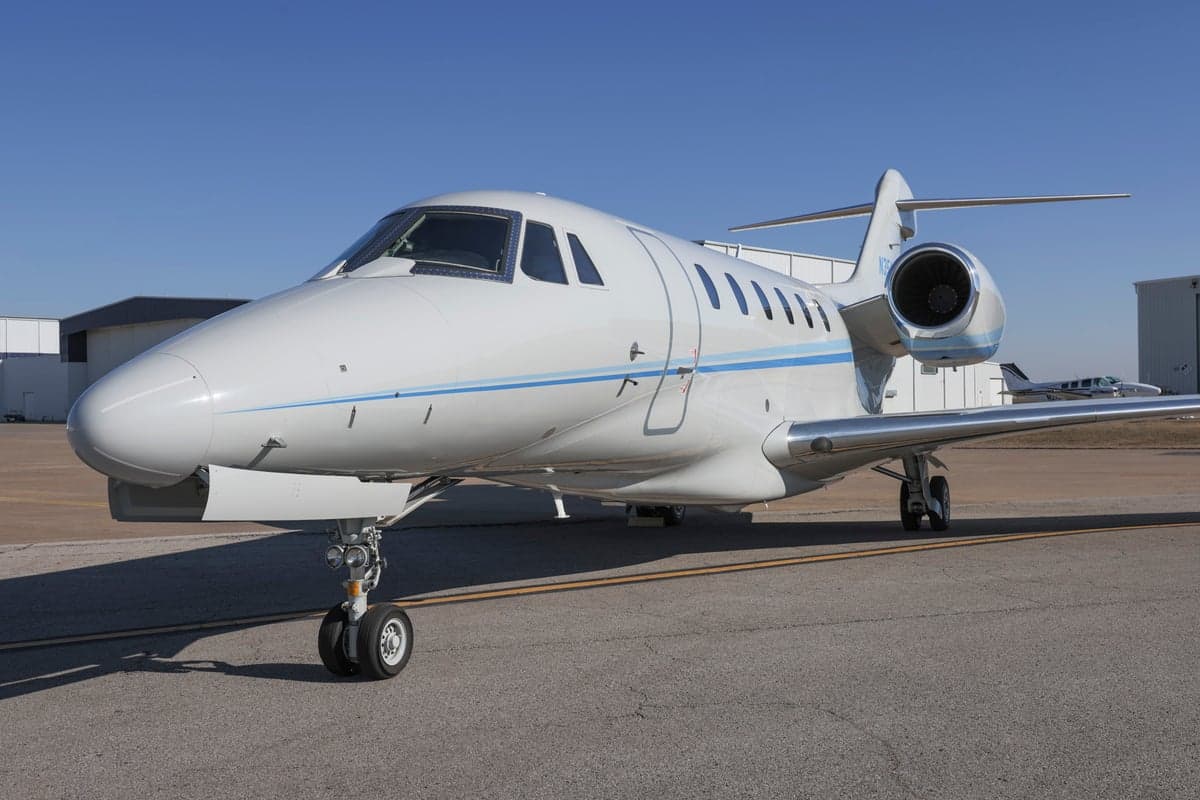 A Citation CJ3 aircraft with a blue and white paint scheme parked on the tarmac, front view.