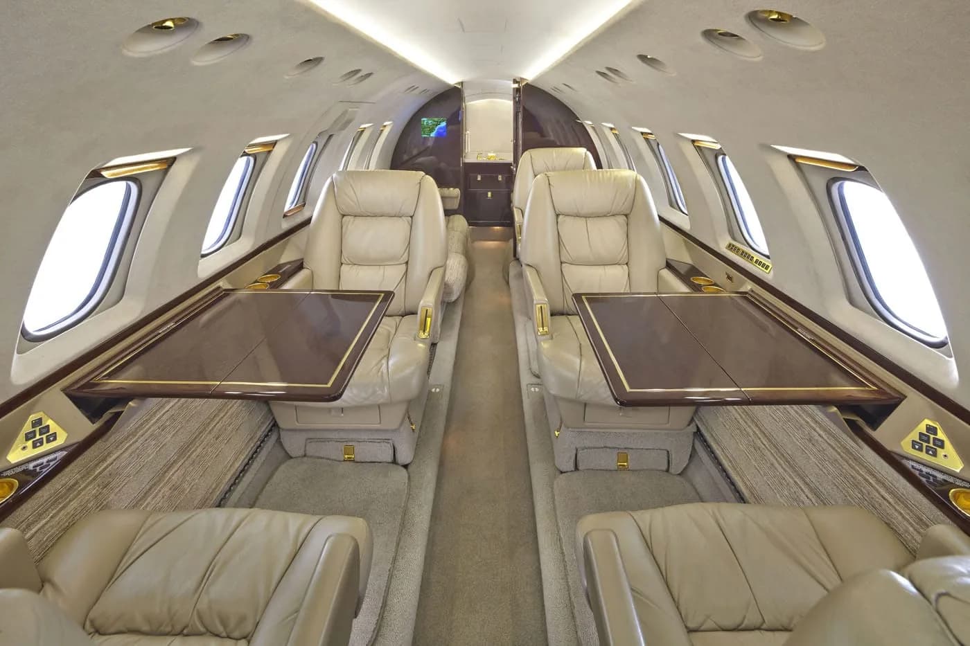 The spacious interior of a private jet cabin, featuring opposing pairs of cream leather seats with fold-out tables.