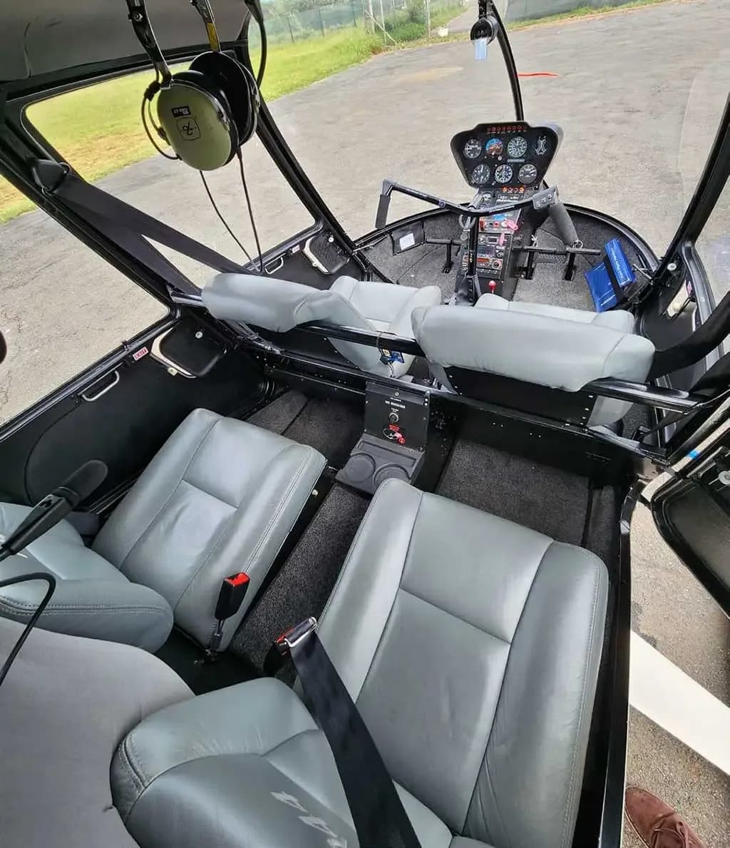 The gray leather interior of a Robinson R44 helicopter, showing four seats and the instrument panel in the front.