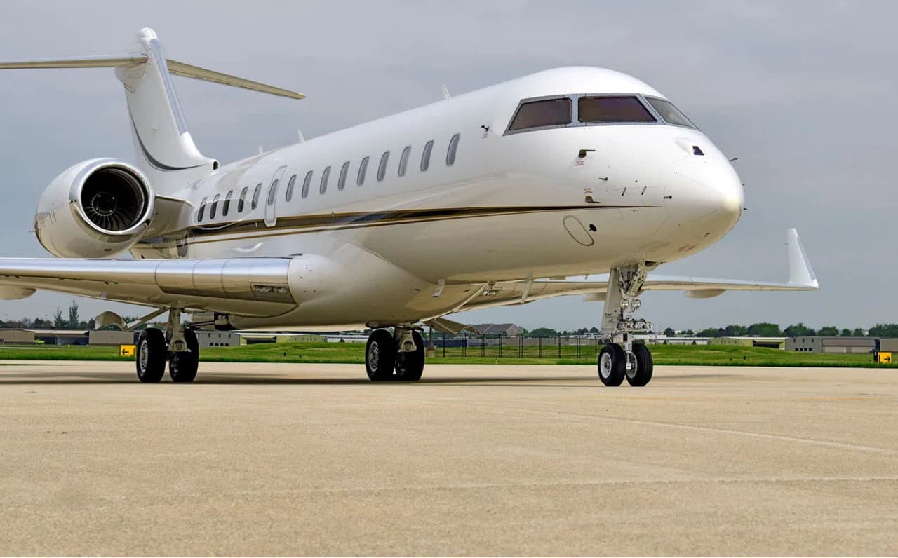 A white business jet with a gold stripe is parked on a tarmac, viewed from the front-right.