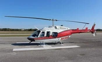 A red and white Bell 206 helicopter sits on the tarmac.
