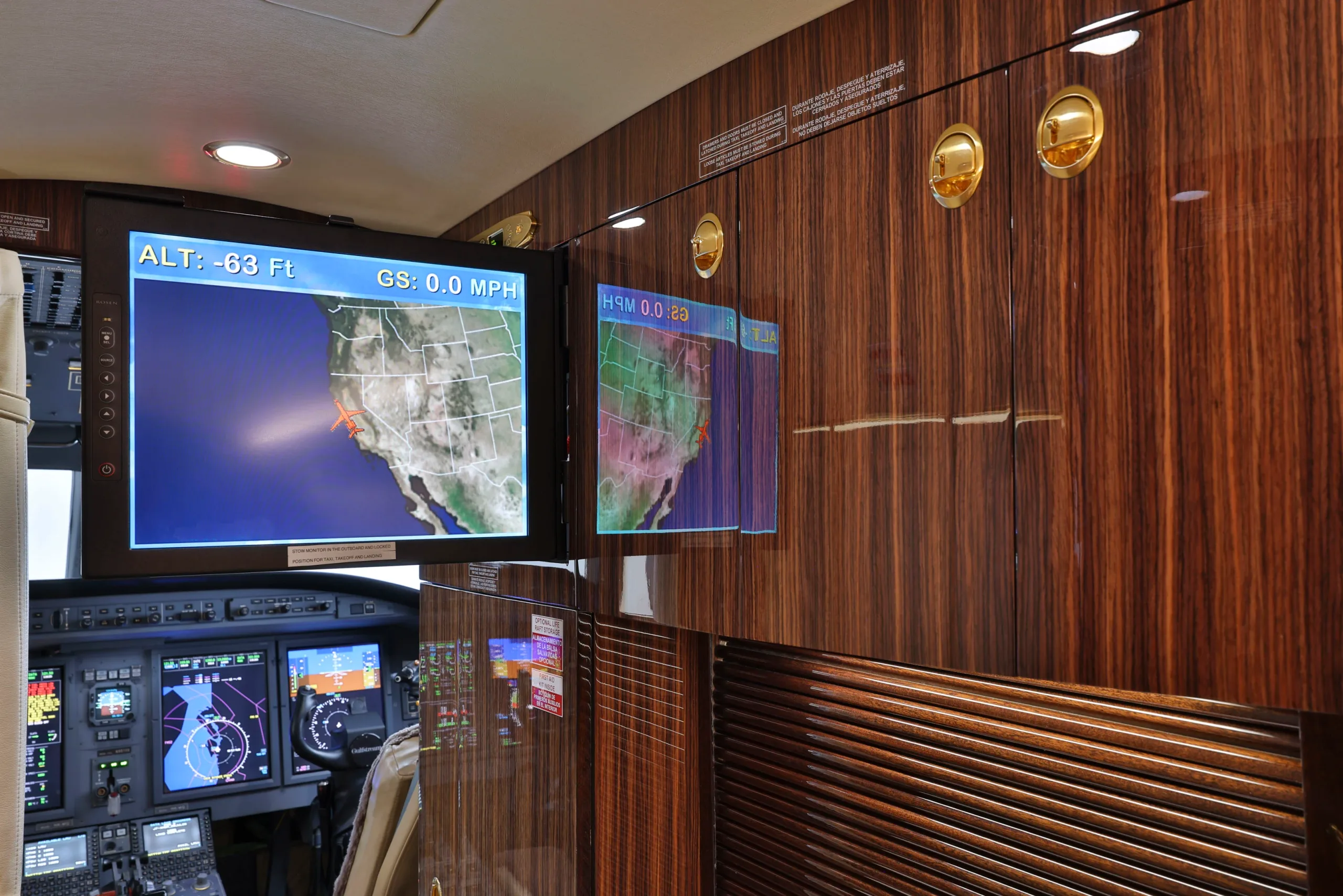 Aircraft cabin interior showing two monitors displaying a map of the United States and rich wood paneling.