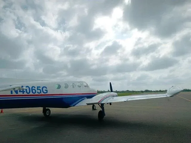 A side view of the front section and right wing of a white and blue Cessna 340 aircraft on an airfield.