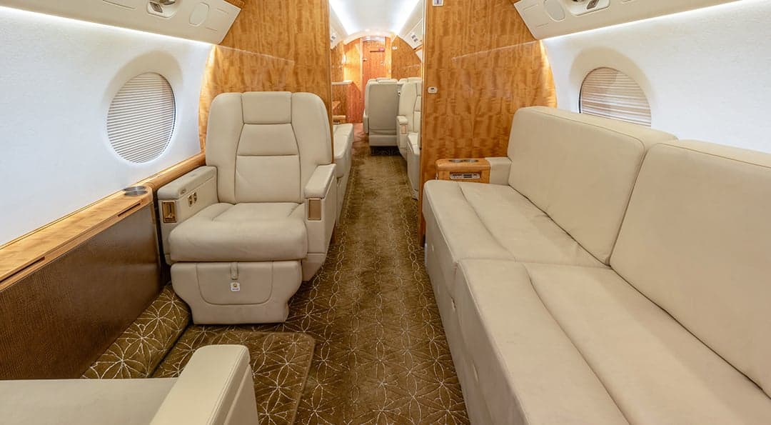 The aircraft's interior features cream-colored leather seats and wood paneling.
