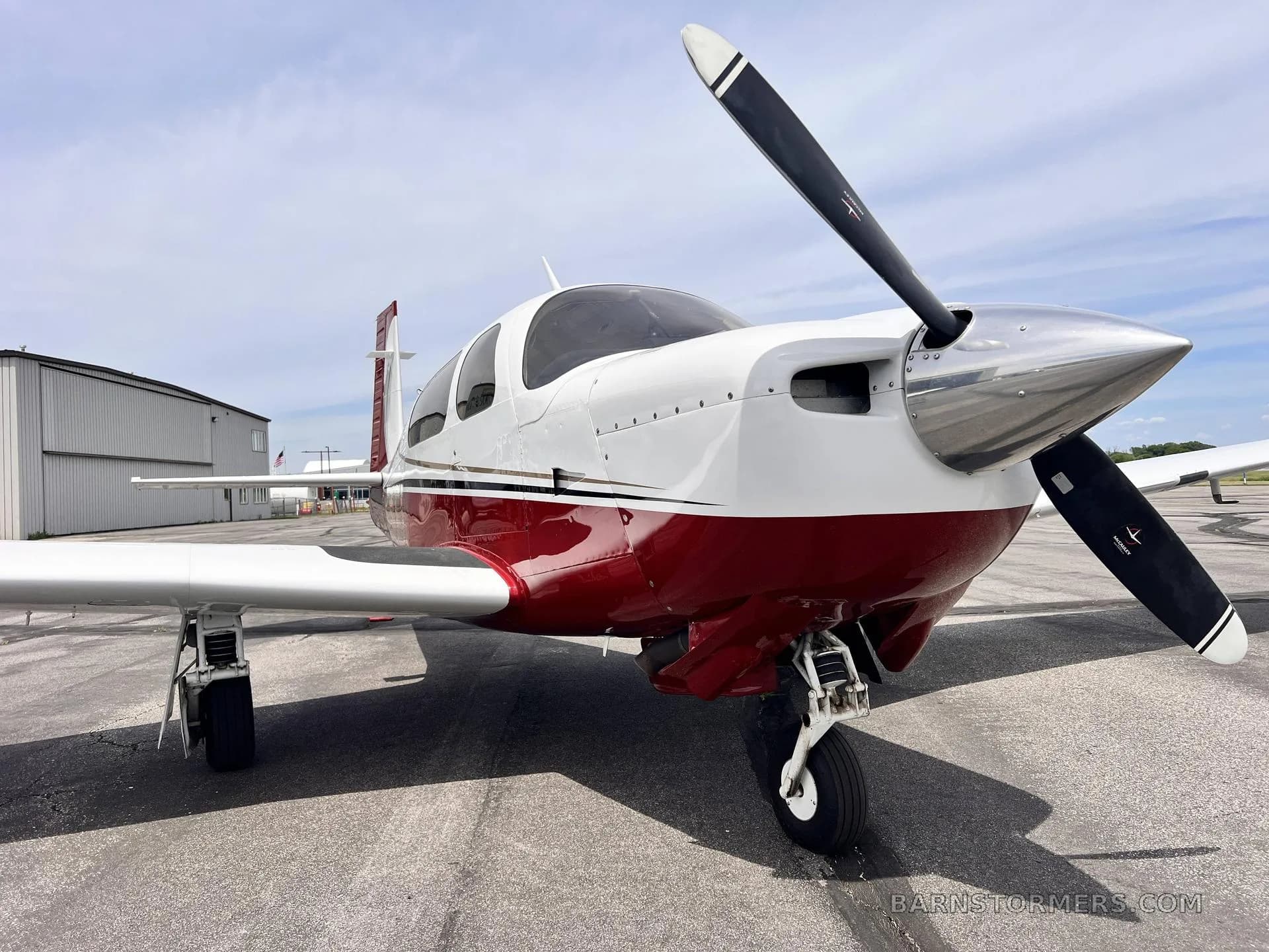 A front-quarter view of a white and red single-engine propeller aircraft on an asphalt tarmac.