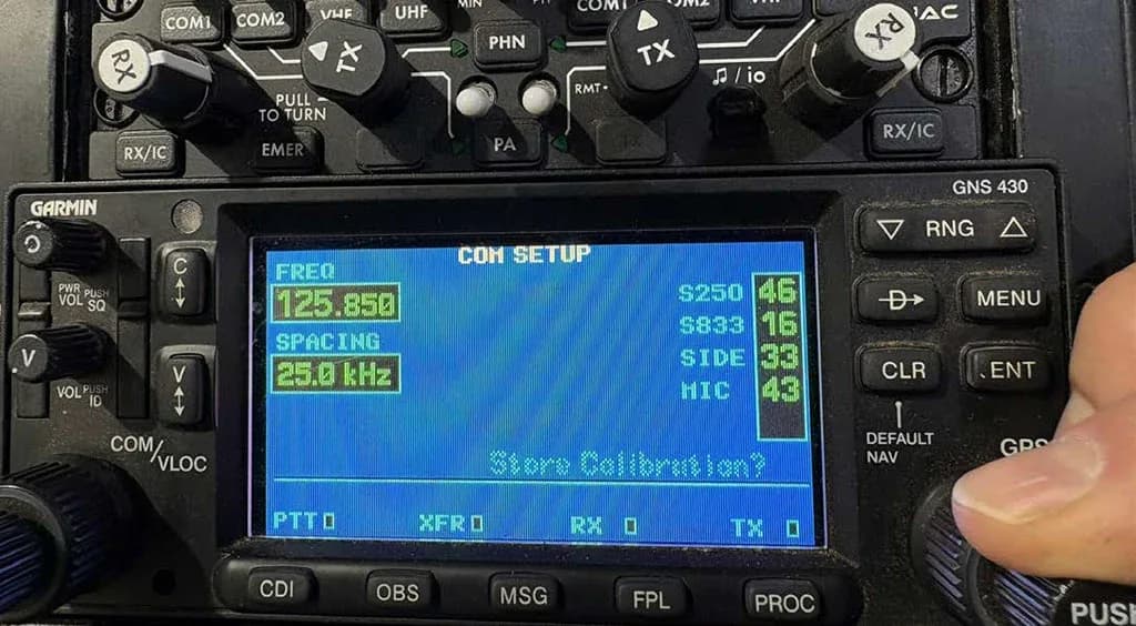 A close-up of a Garmin GNS 430 avionics unit displaying 'COM SETUP' with frequency and spacing information.