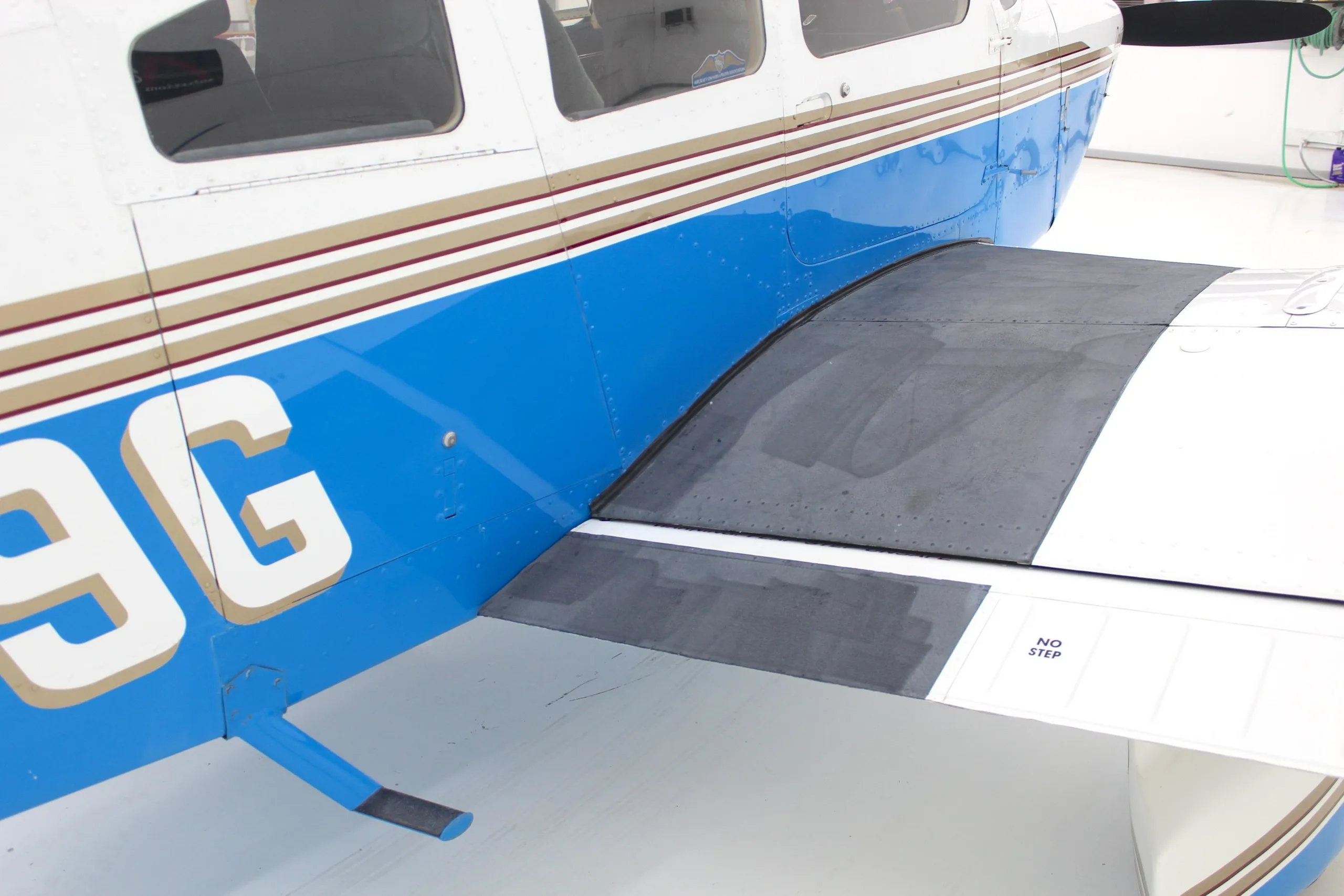 A close-up view of the wing root and lower fuselage of the white and blue Piper Dakota aircraft.