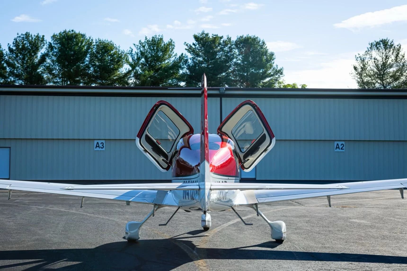 Rear view of a red and white Cirrus SR22 aircraft (N412CP) with its doors open, parked in front of a hangar.
