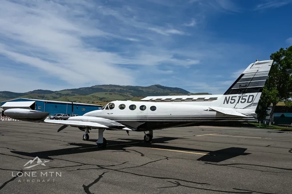 A side view of the white and black twin-engine aircraft, N515D, showing its tail and fuselage, parked on an airfield.